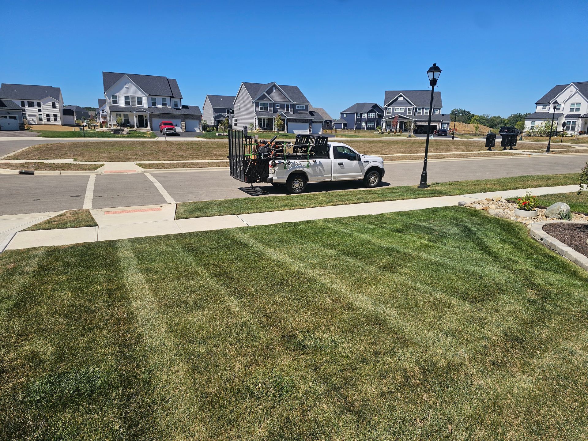 Lawn care truck on suburban street, freshly mowed lawn, houses in the background, blue sky.