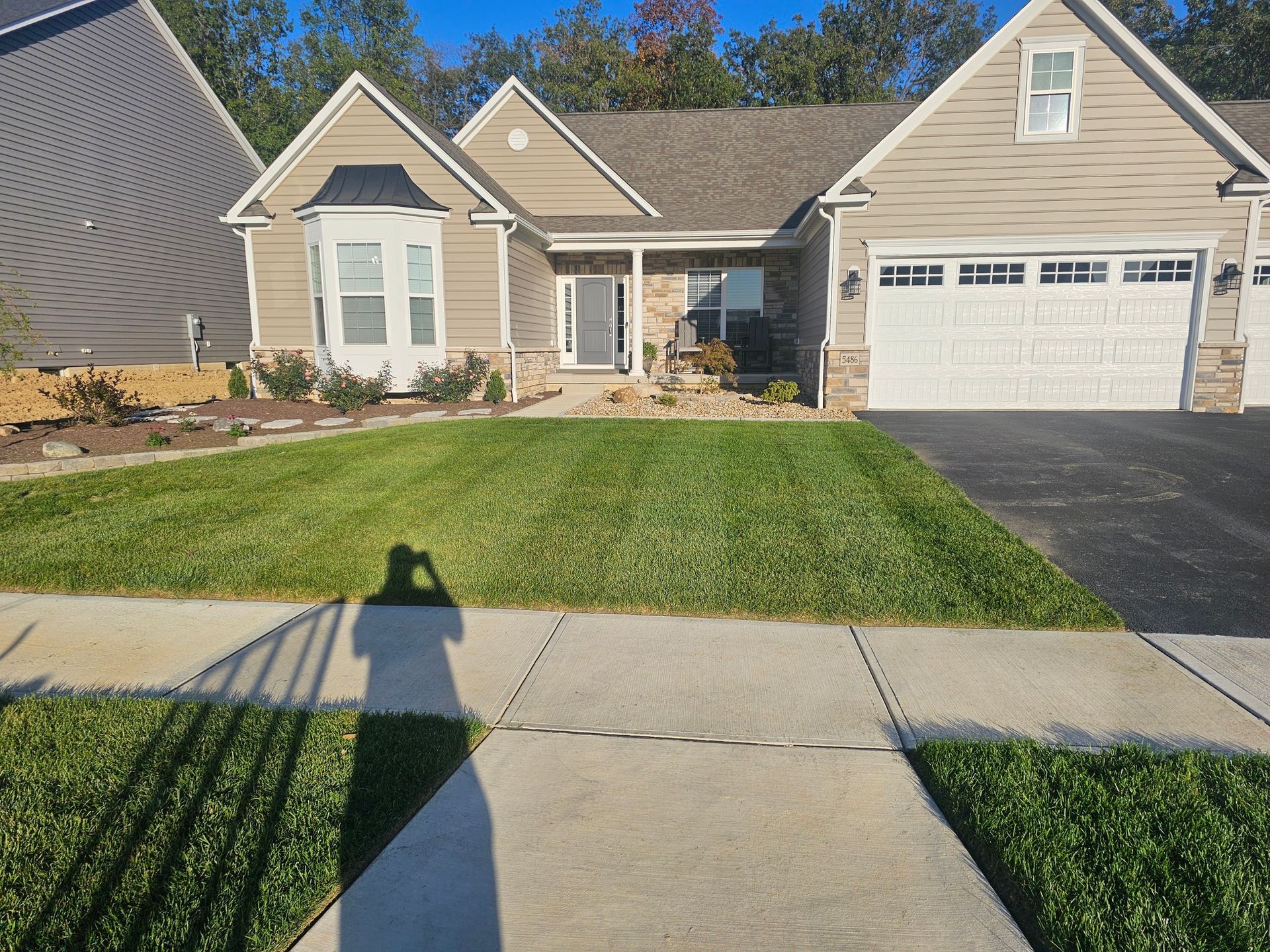 Tan suburban house with manicured lawn, blue sky. A shadow of a person taking a picture.