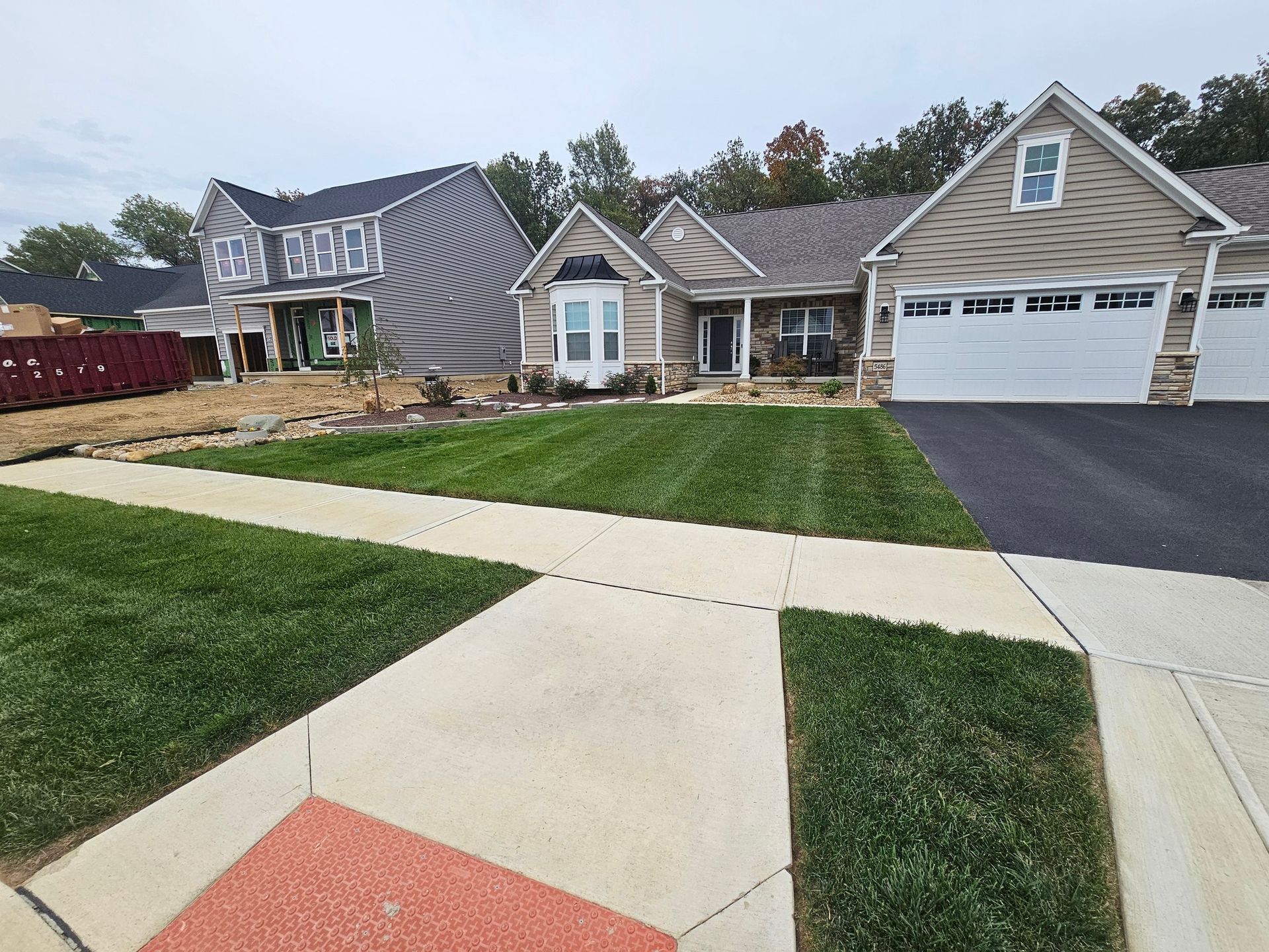 Houses with manicured lawns and a paved sidewalk under a cloudy sky.
