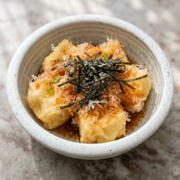 Small bowl of tofu topped with grated garnish and shredded seaweed on a marble surface