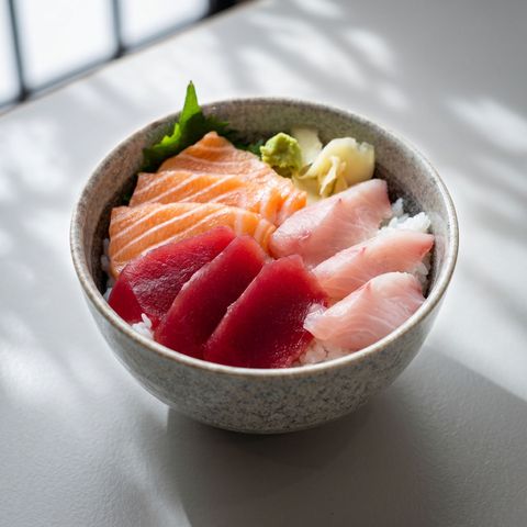 Bowl of assorted sashimi on rice with wasabi, lit by soft window light