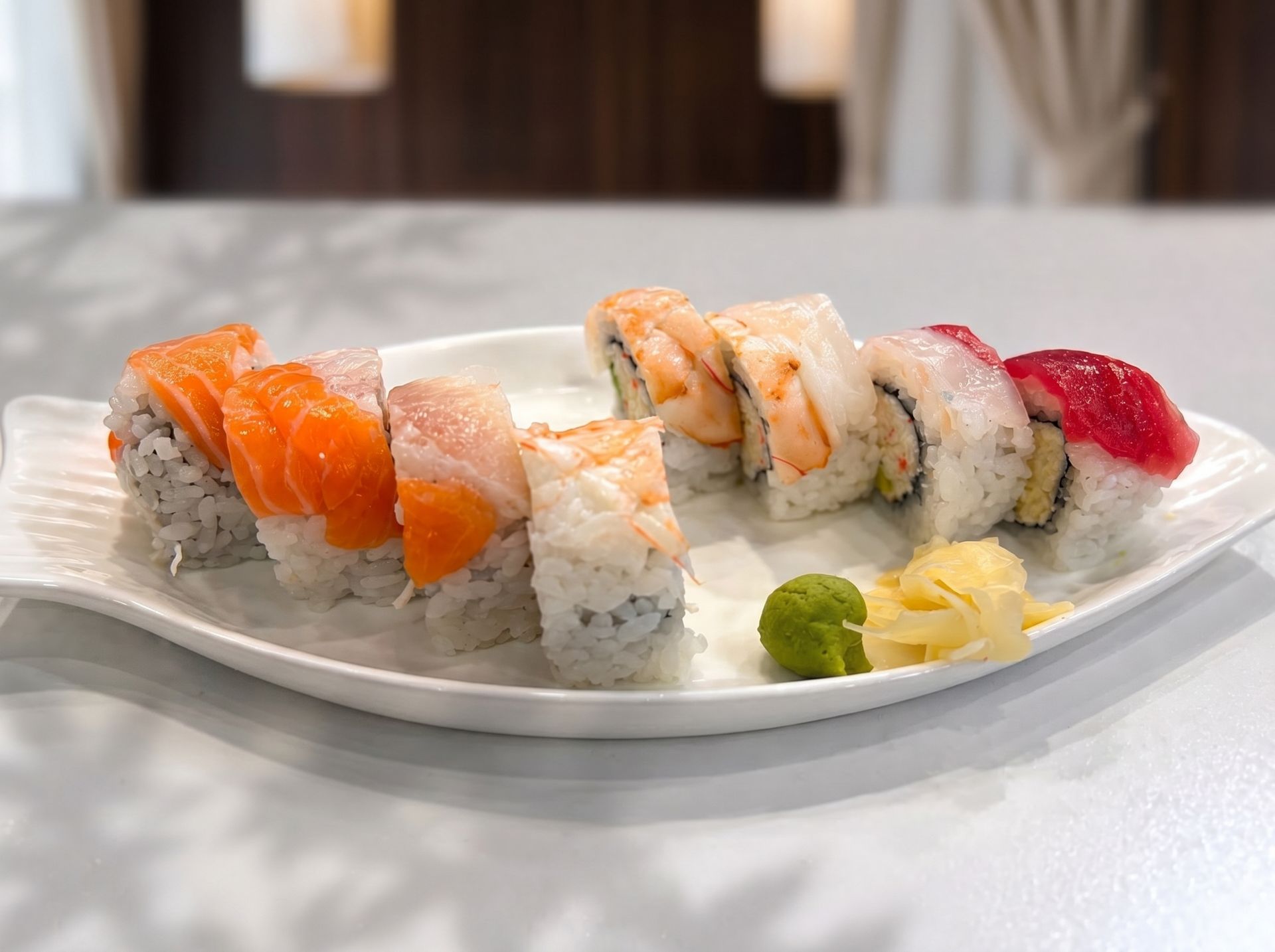 Sushi rolls and nigiri on a white plate with wasabi and pickled ginger