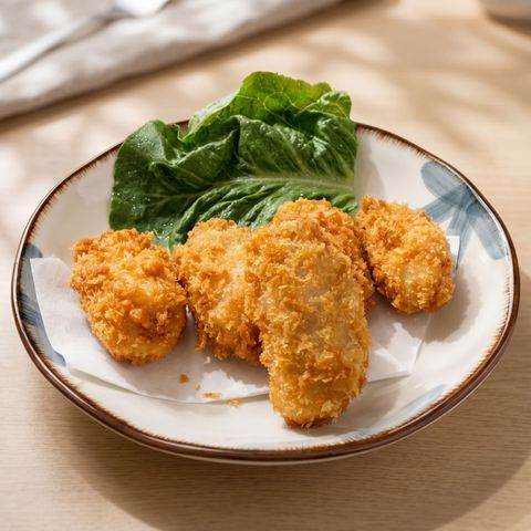 Plate of crispy breaded fried chicken pieces with green leafy garnish on a white dish