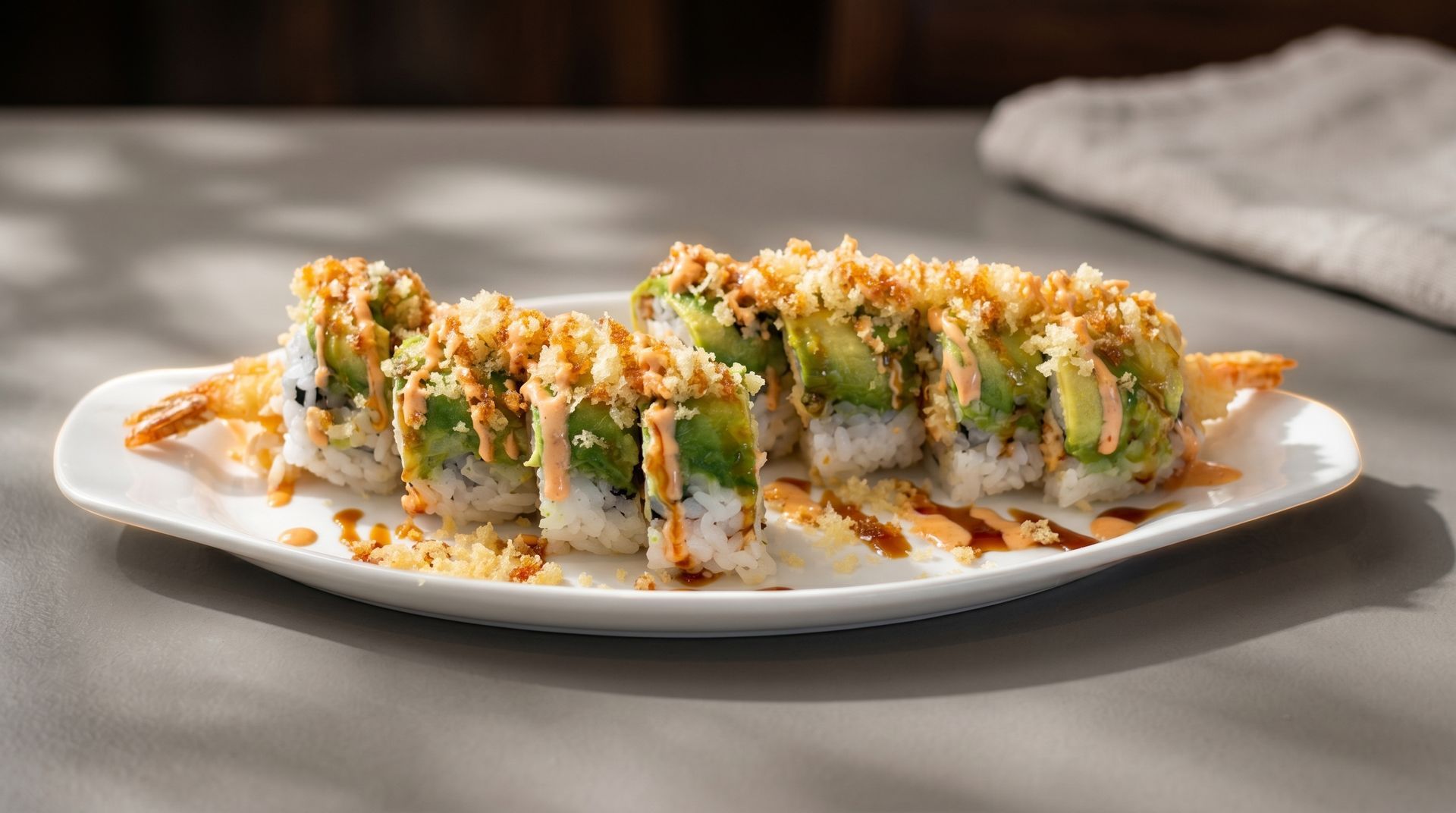 Sushi rolls topped with green sauce and crunchy bits on a white plate