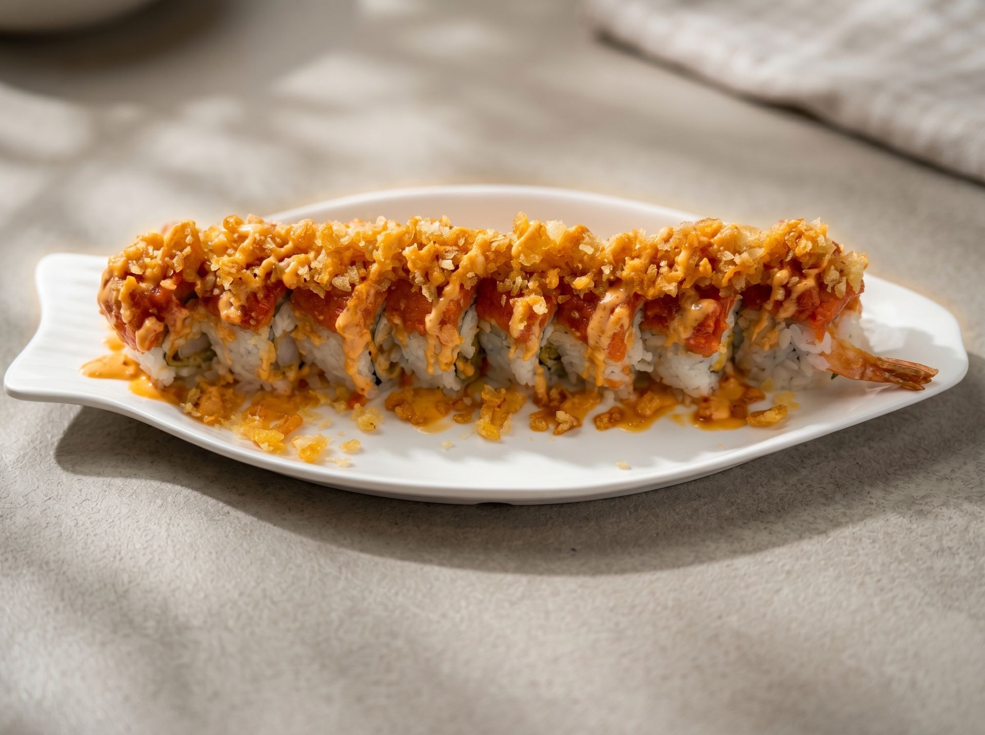 Sushi roll topped with orange sauce and crunchy crumbs on a white platter