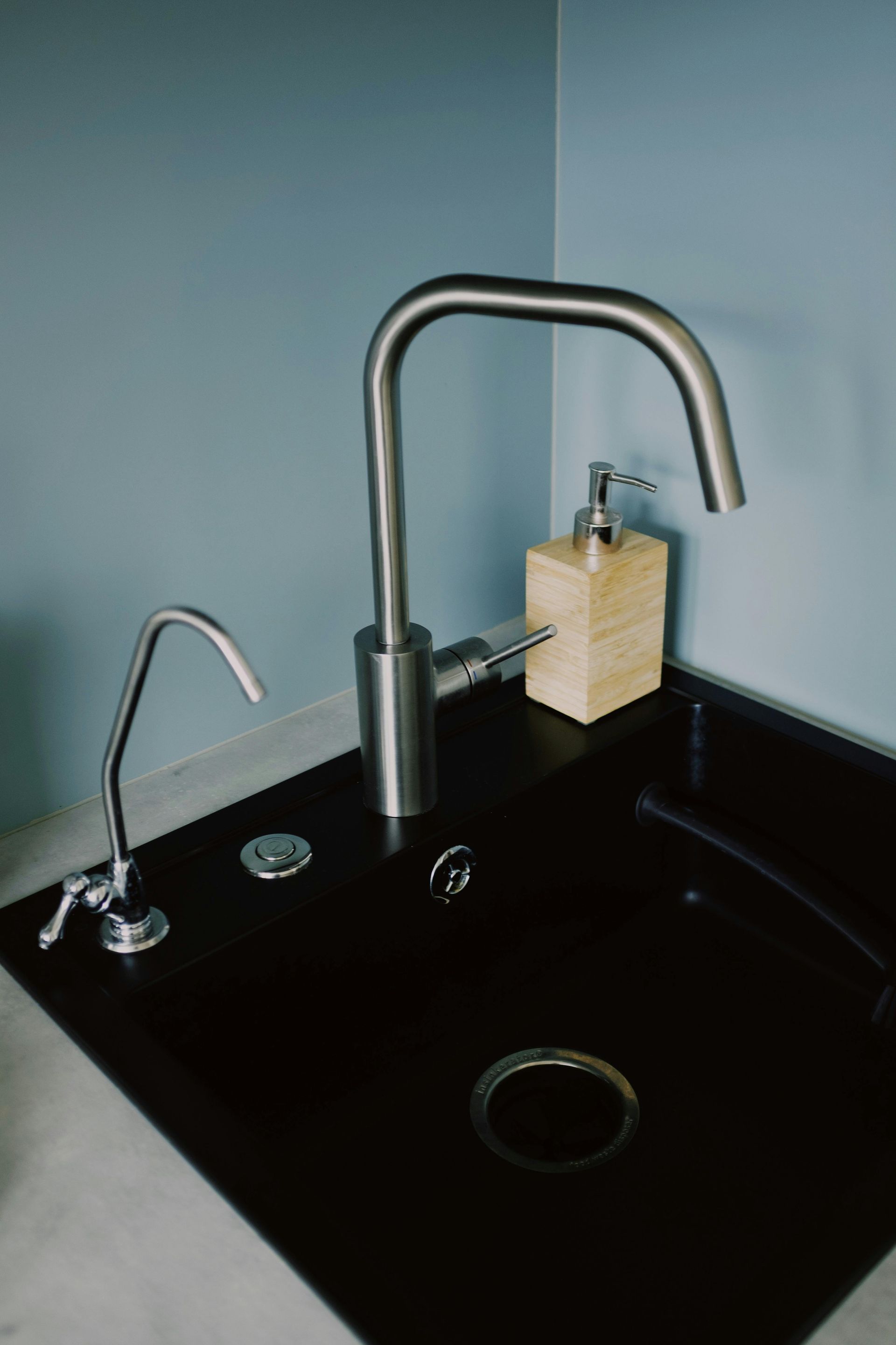 A black kitchen sink with a tall silver faucet, a smaller drinking water faucet.