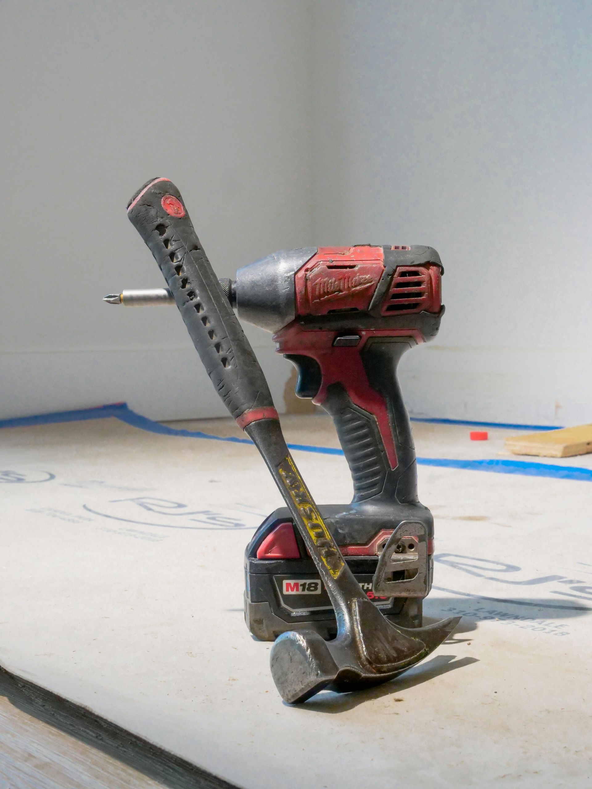 Hammer leaning on a red and black drill on a construction surface.