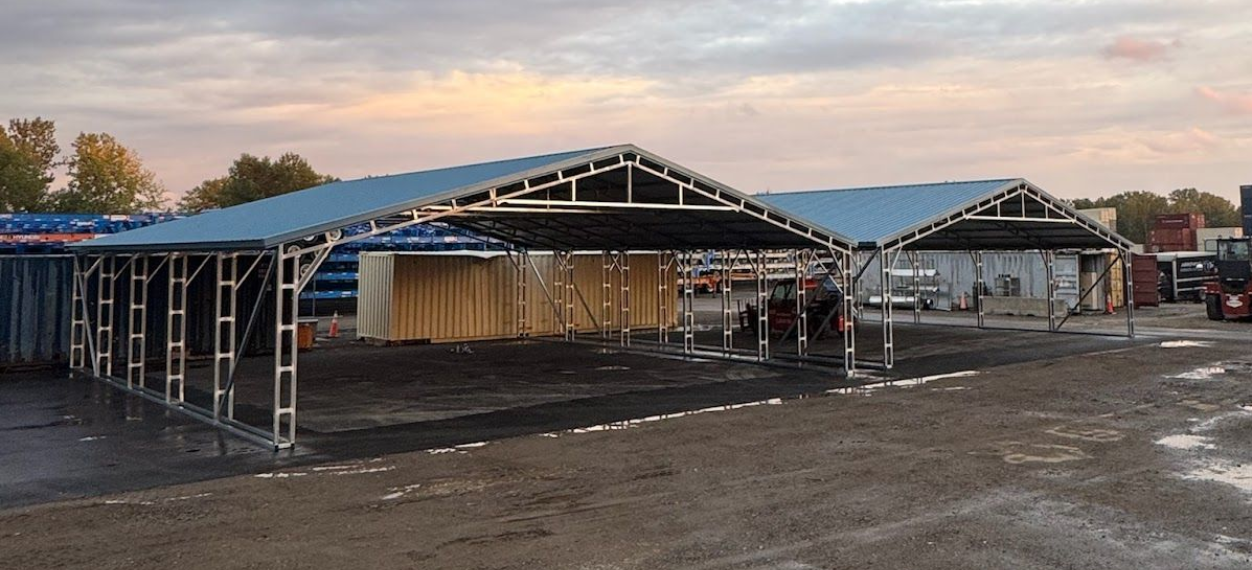 Two metal carports on a gravel lot; gray sky.