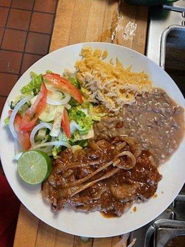 A plate of food with meat , beans , rice and a salad on a wooden table.