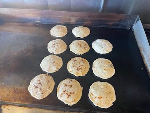 A bunch of pancakes are cooking on a grill.