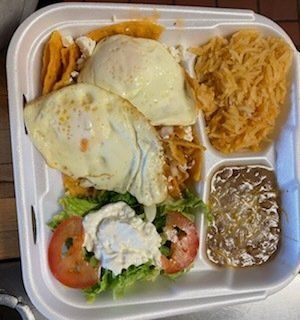 A styrofoam container filled with fried eggs , noodles , tomatoes and salsa.