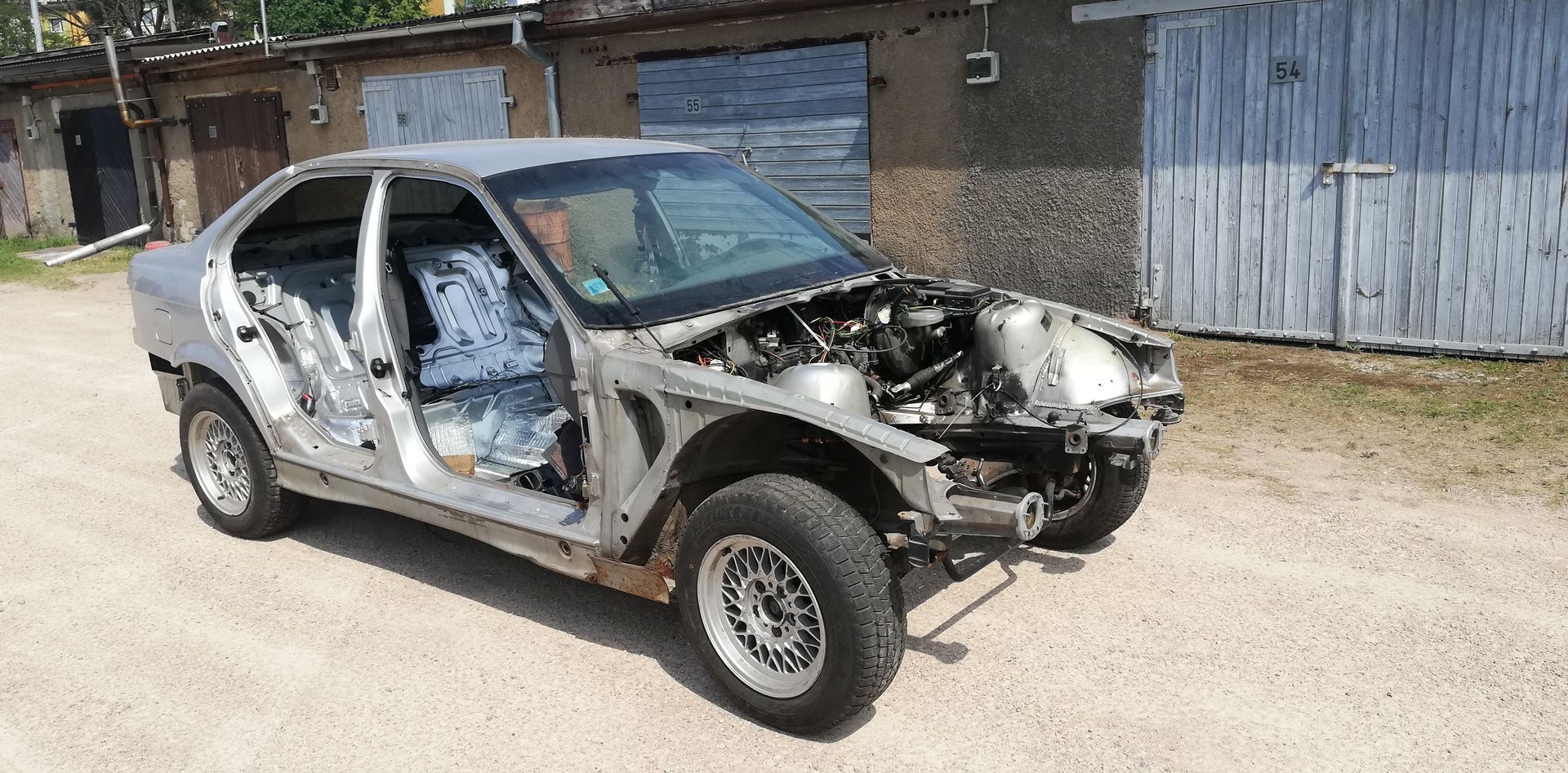 A wrecked car is parked on a dirt road in front of a garage.