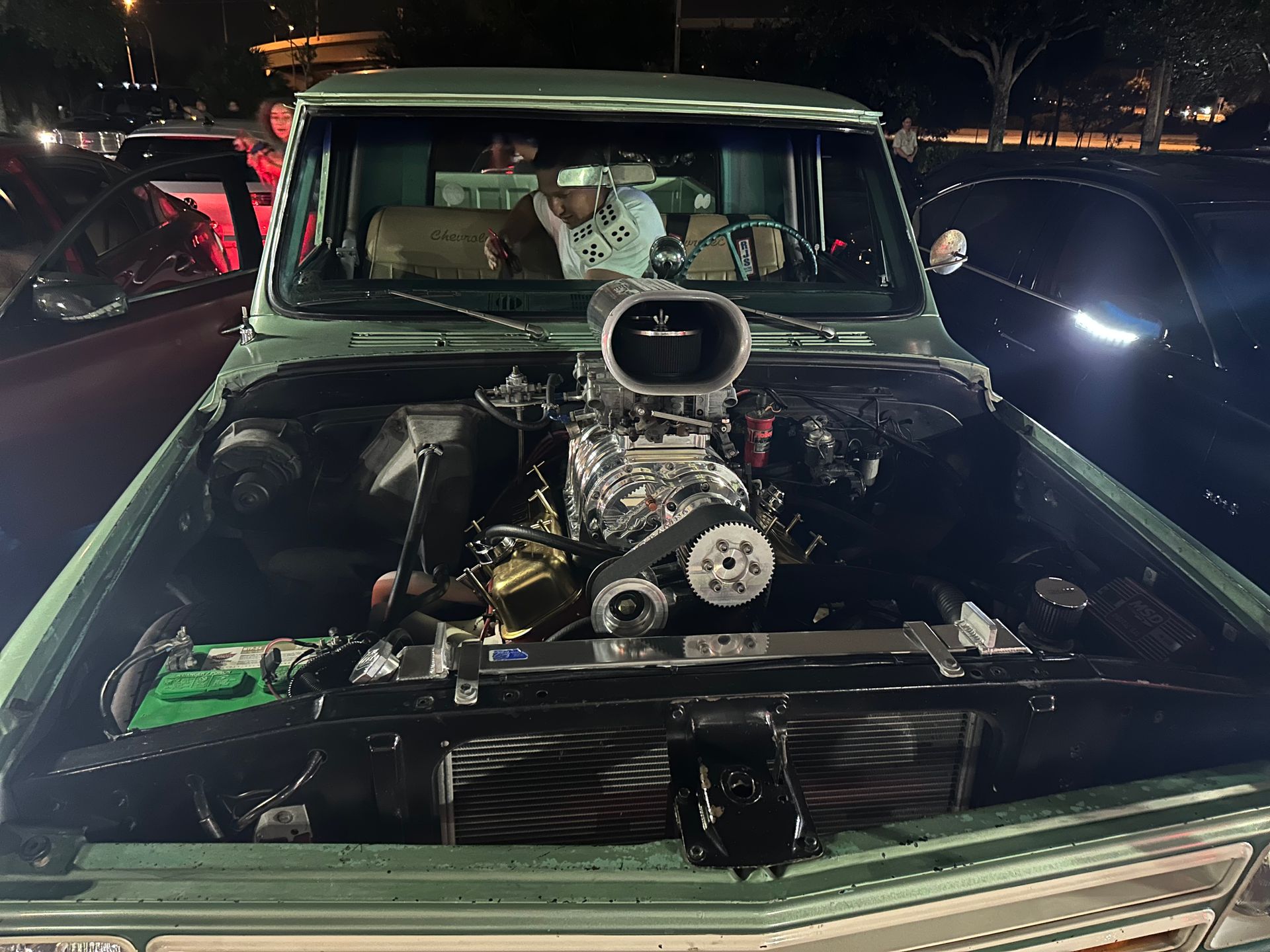 A man is sitting in the driver 's seat of a green truck with the hood open.