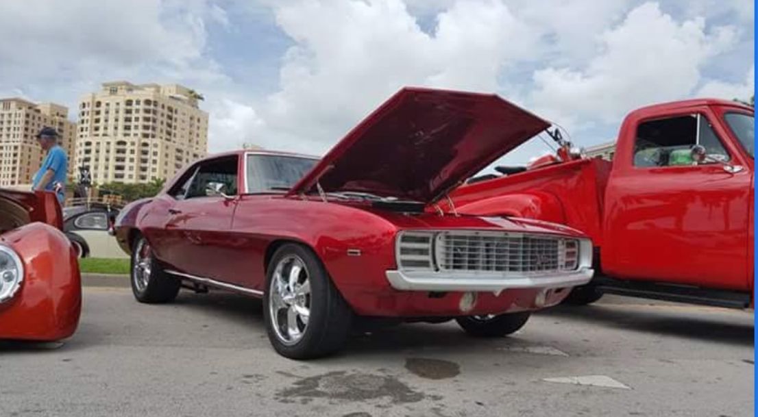 A red car with the hood up is parked next to a red truck