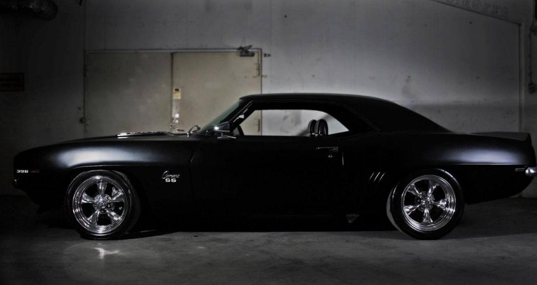 A black car with chrome wheels is parked in a garage.