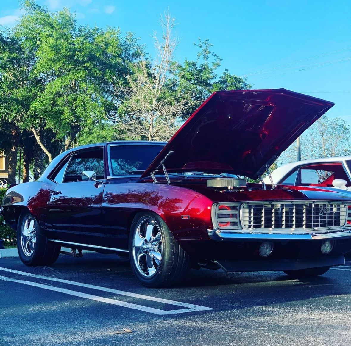 A red car with the hood up is parked in a parking lot
