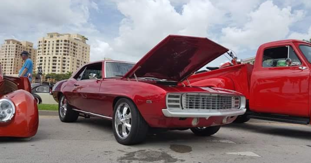 A red car with the hood up is parked next to a red truck.