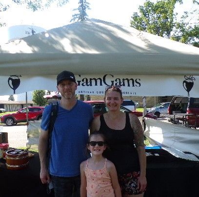 Family stands in front GamGams tent at Elk River outdoor market.