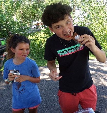 Two kids outside GamGams booth eating chocolate bars. Boy is laughing, girl is smiling.