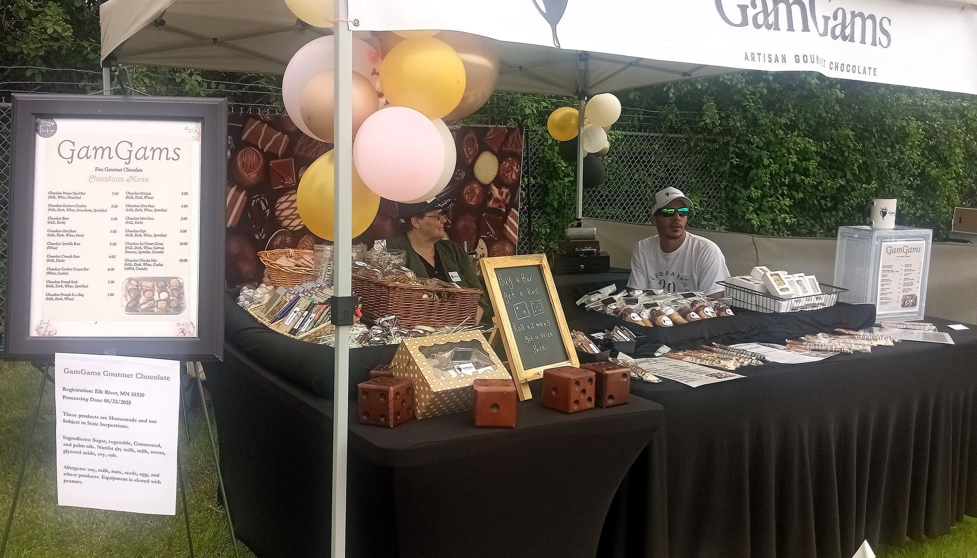 A vendor booth selling baked goods at an outdoor event. Balloons, signs, and a person behind the counter.