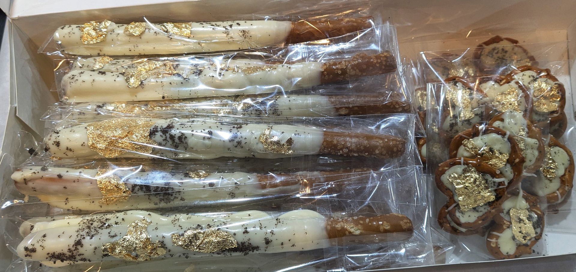 GamGams Pretzel rods and rounds dipped in white chocolate, gold leaf, and sprinkles in a box.