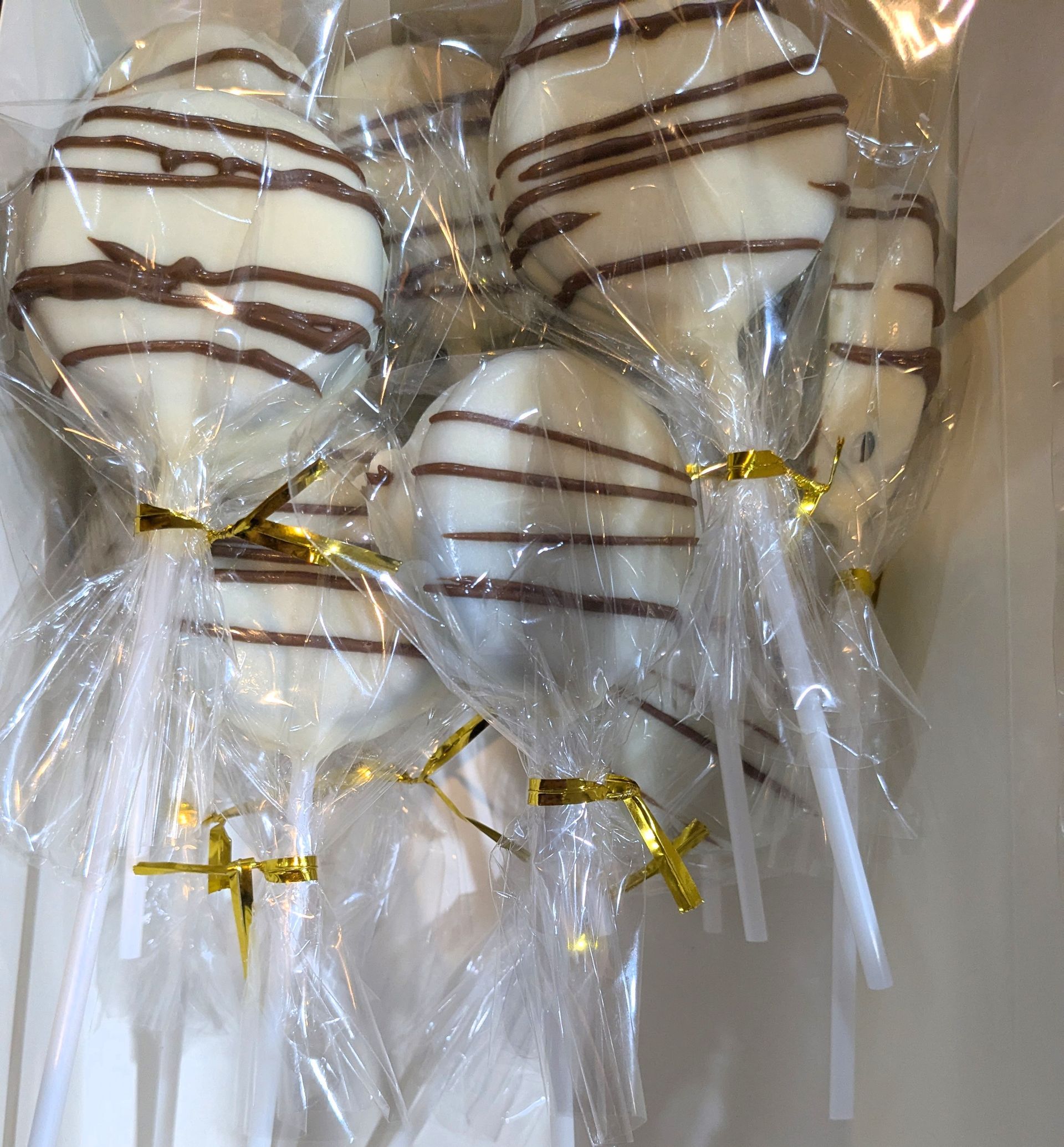 GamGams White chocolate cake pops with dark chocolate drizzle, wrapped in cellophane and tied with gold ribbons.