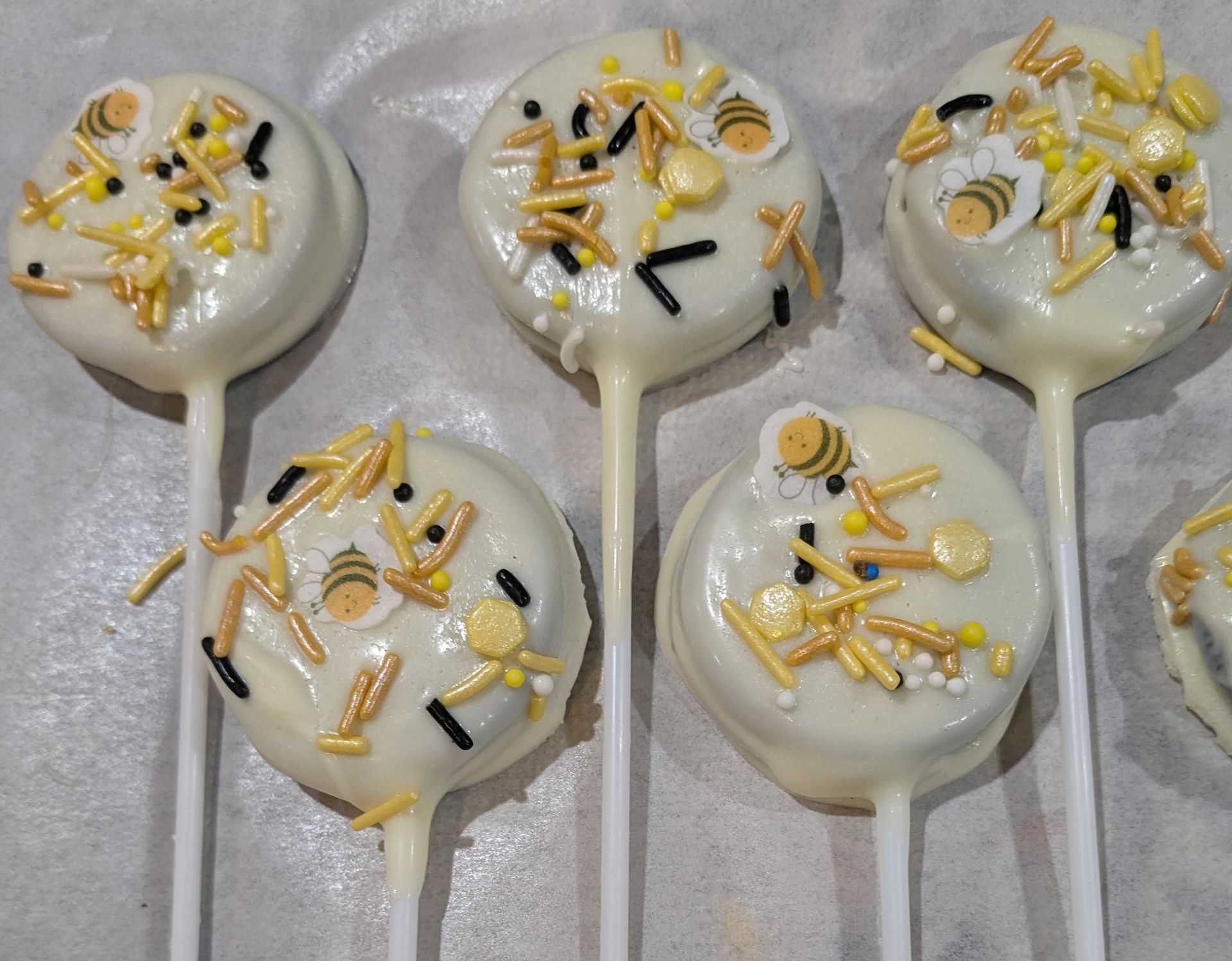 Oreo cookie pops dipped in white chocolate, decorated with bee sprinkles and small bee images. Get it at GamGams Booth.