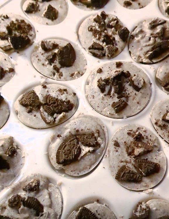 Close-up of cookies and cream treats in a white muffin tin, speckled with dark cookie pieces. GamGams Treats