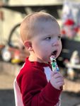 Young child with blonde hair eating a colorful treat, wearing a red and white shirt, outdoors.