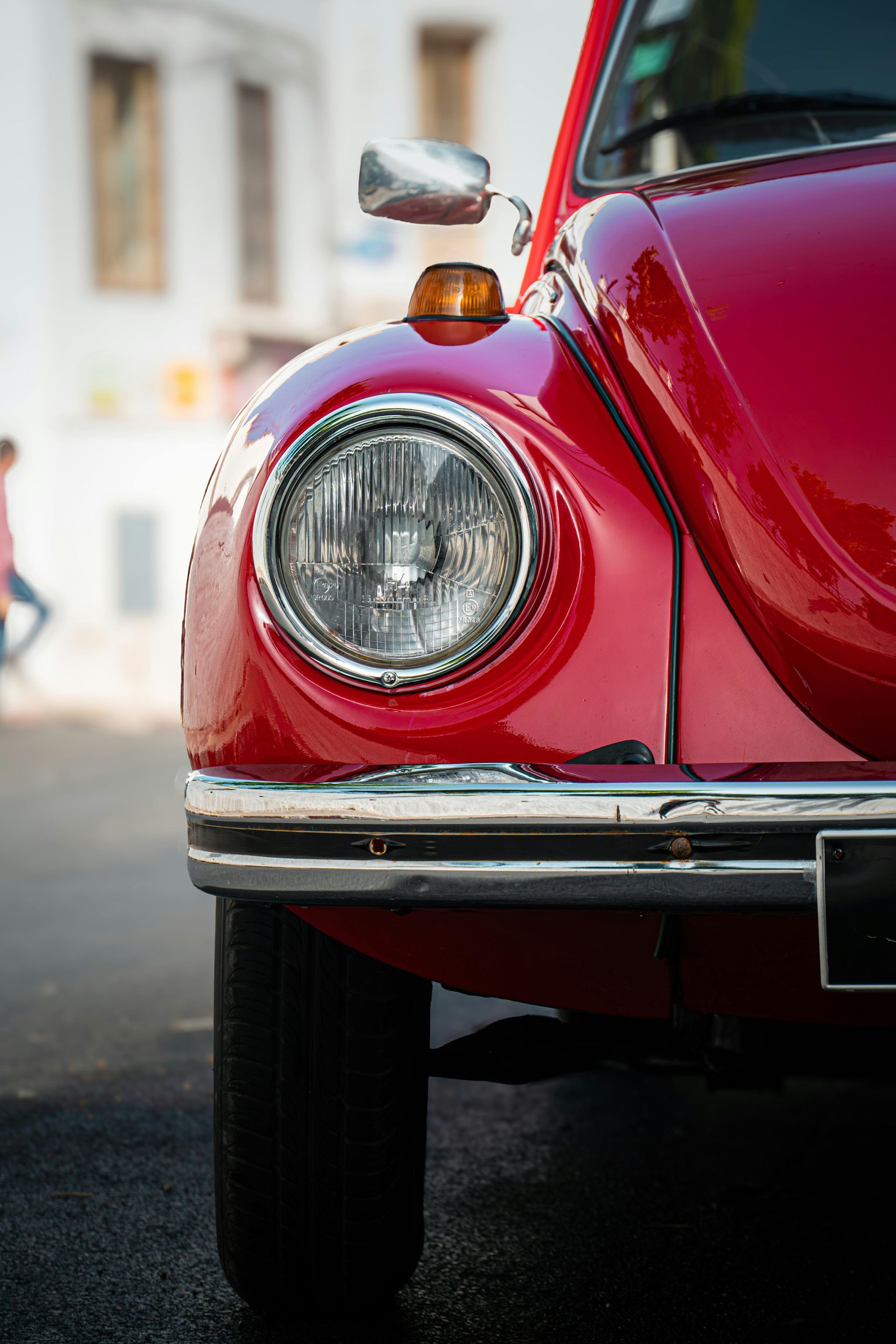 A close-up, front-facing view of a vibrant red Volkswagen Beetle parked on a blurred street.