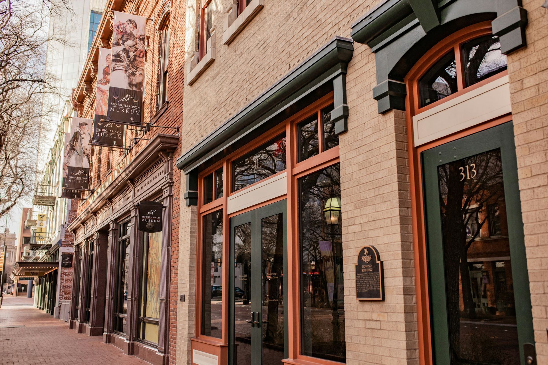 A row of brick buildings on a sidewalk, featuring dark-framed storefront windows and entrance doors with the number 313.