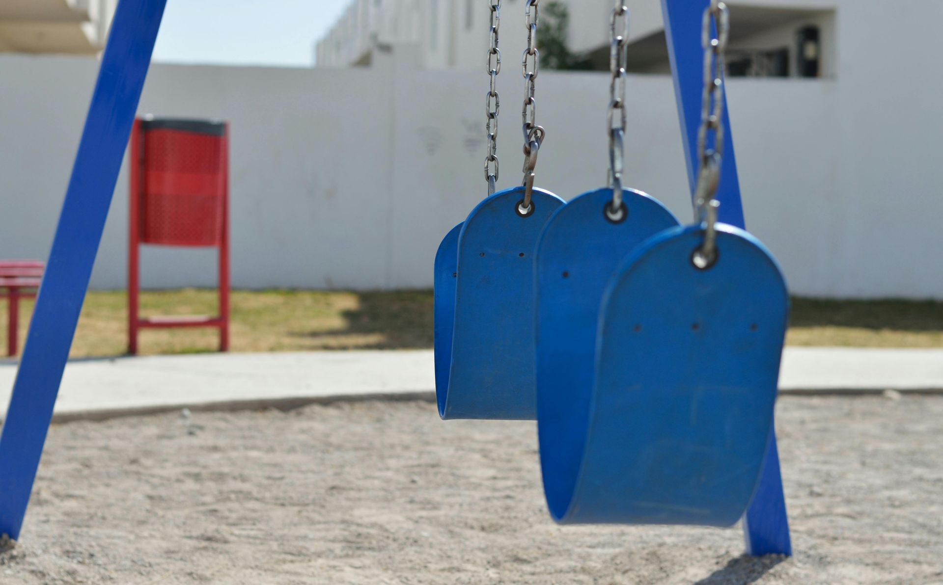 Two blue swing seats hang from chains on a playground set above a sandy ground.