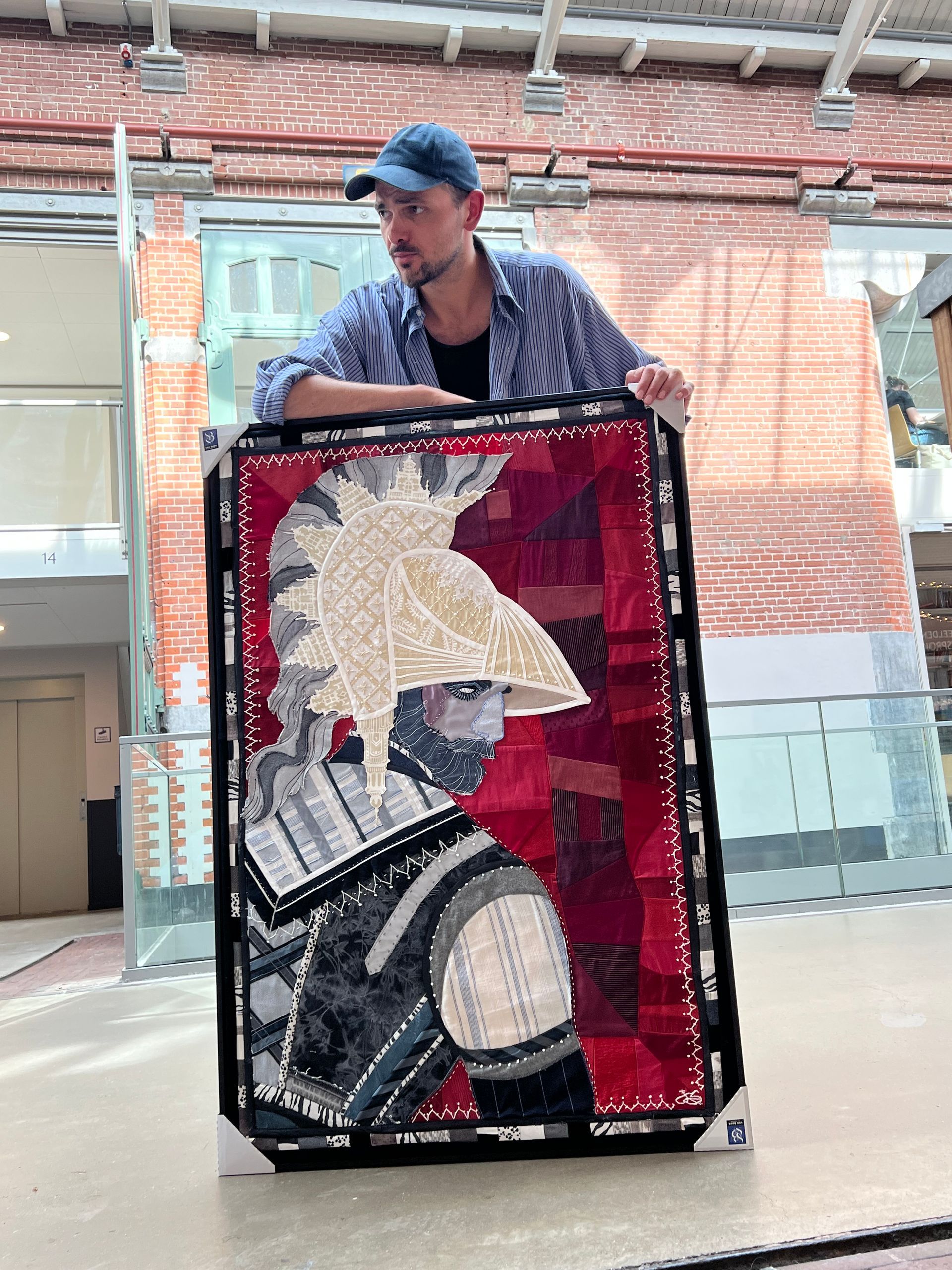 Textile art of a figure in a helmet and armor against a red background.