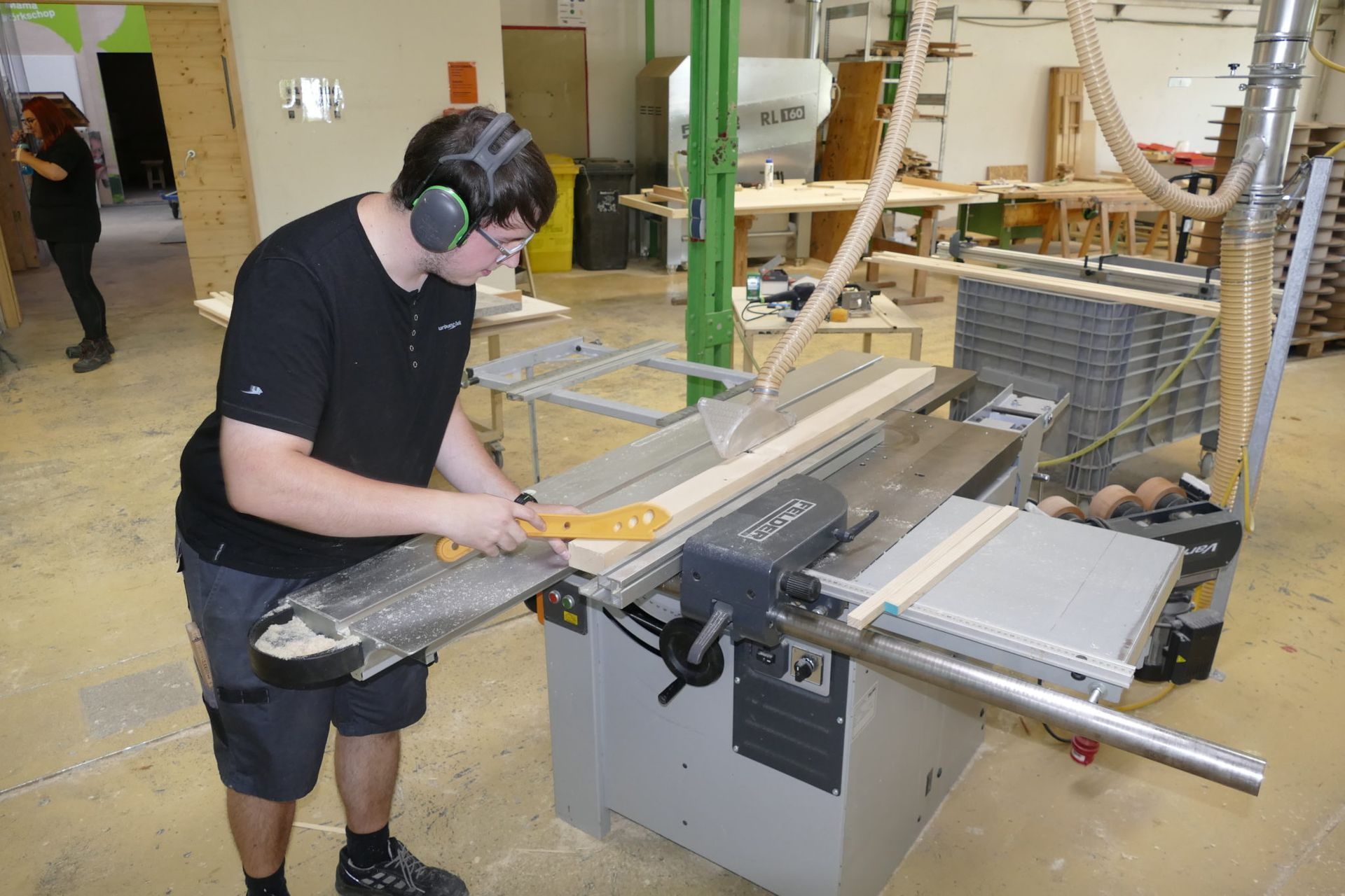 Ein Mann mit Kopfhörern schneidet ein Stück Holz auf einer Tischkreissäge.