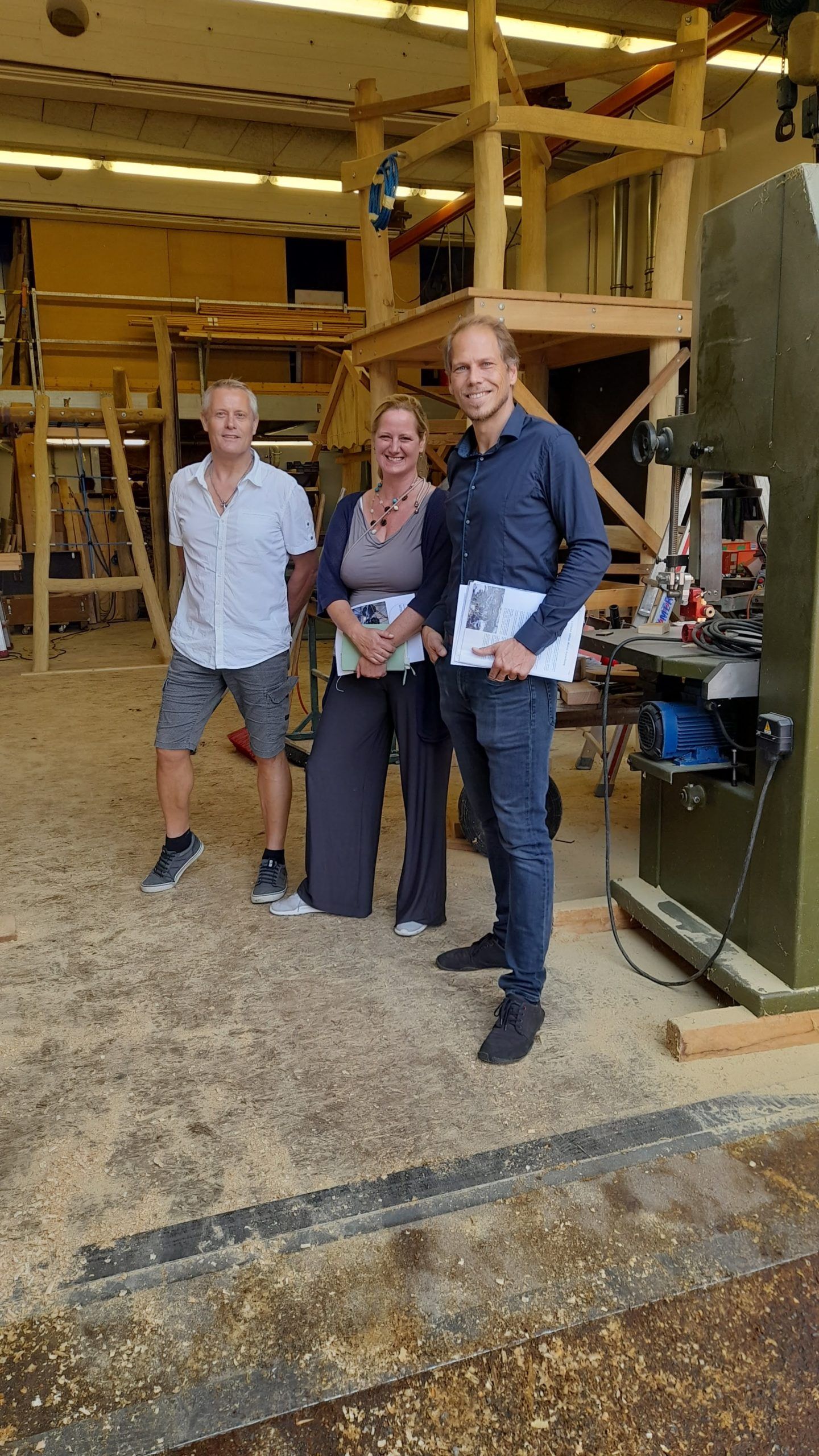 Drei Personen stehen nebeneinander in einer Holzwerkstatt.
