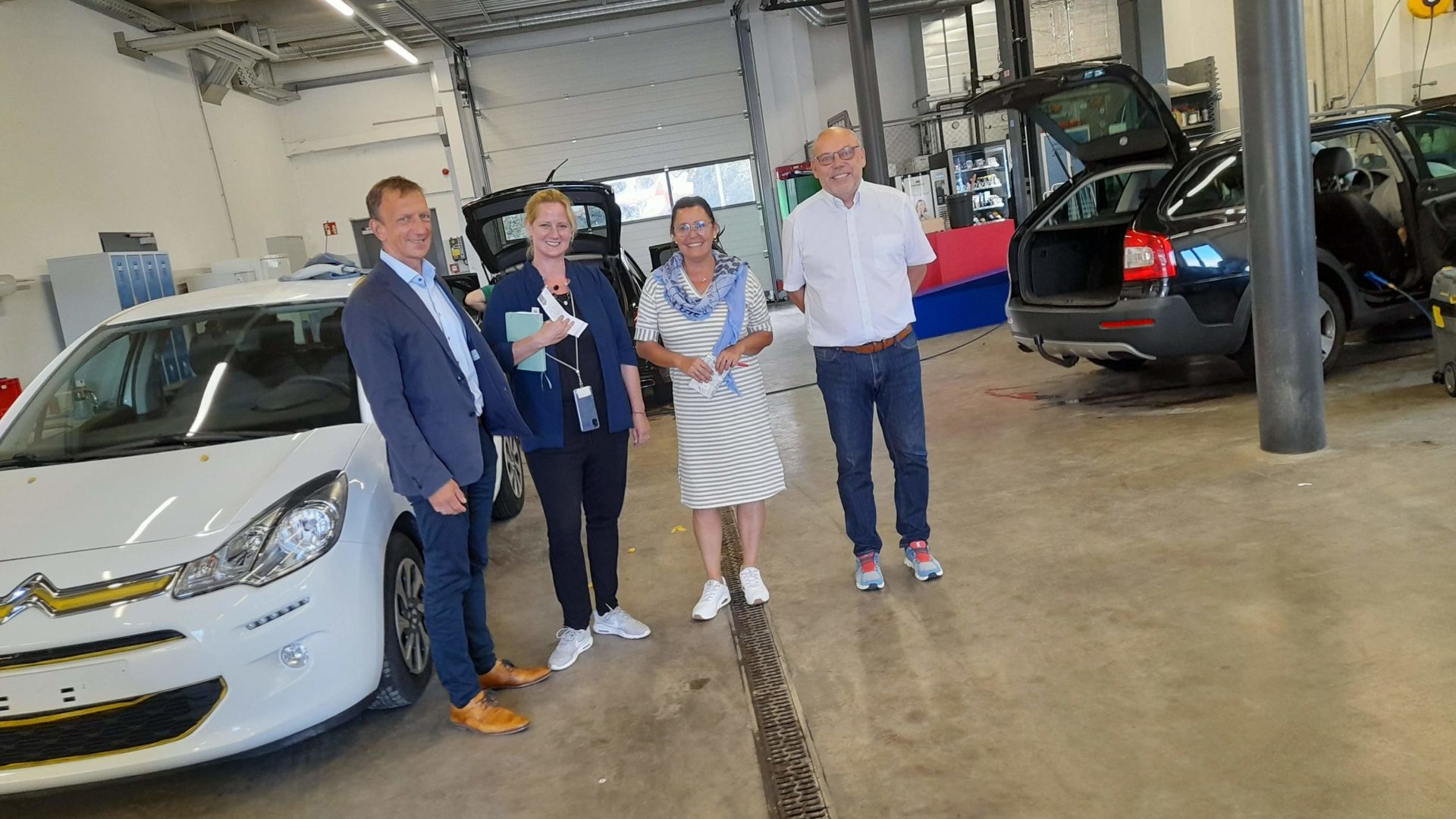 Eine Gruppe von Menschen steht vor einem weißen Auto in einer Garage.