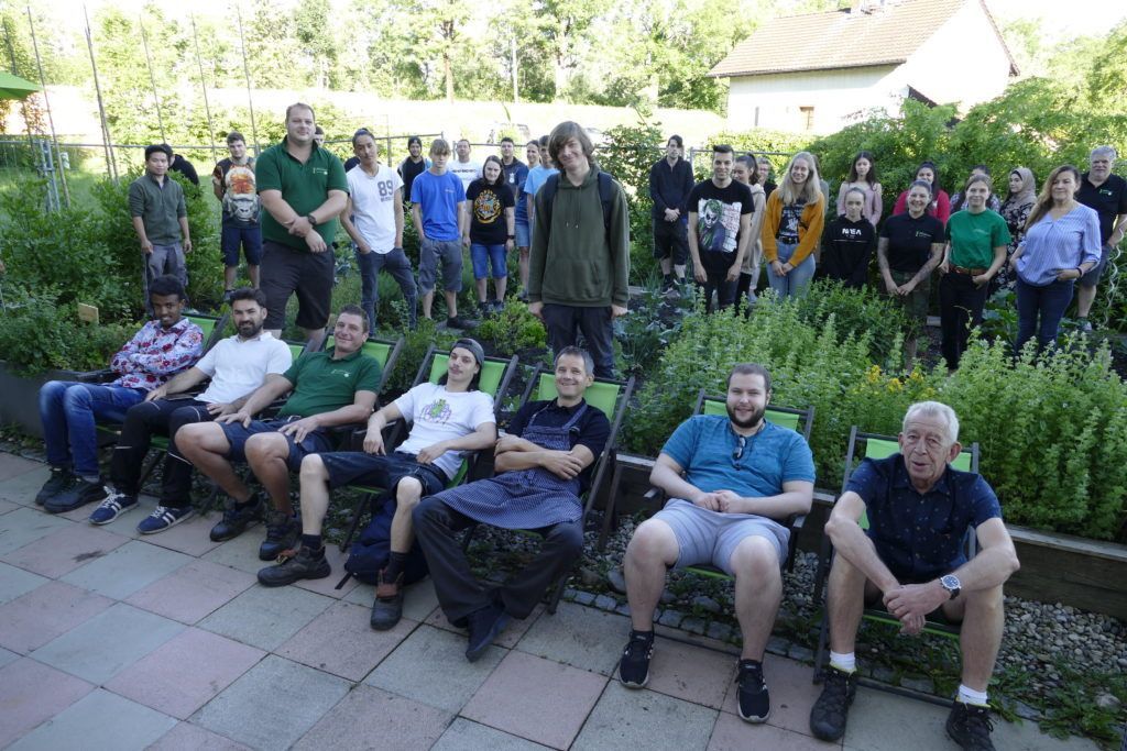 Eine Gruppe von Menschen sitzt auf Stühlen vor einem Haus.