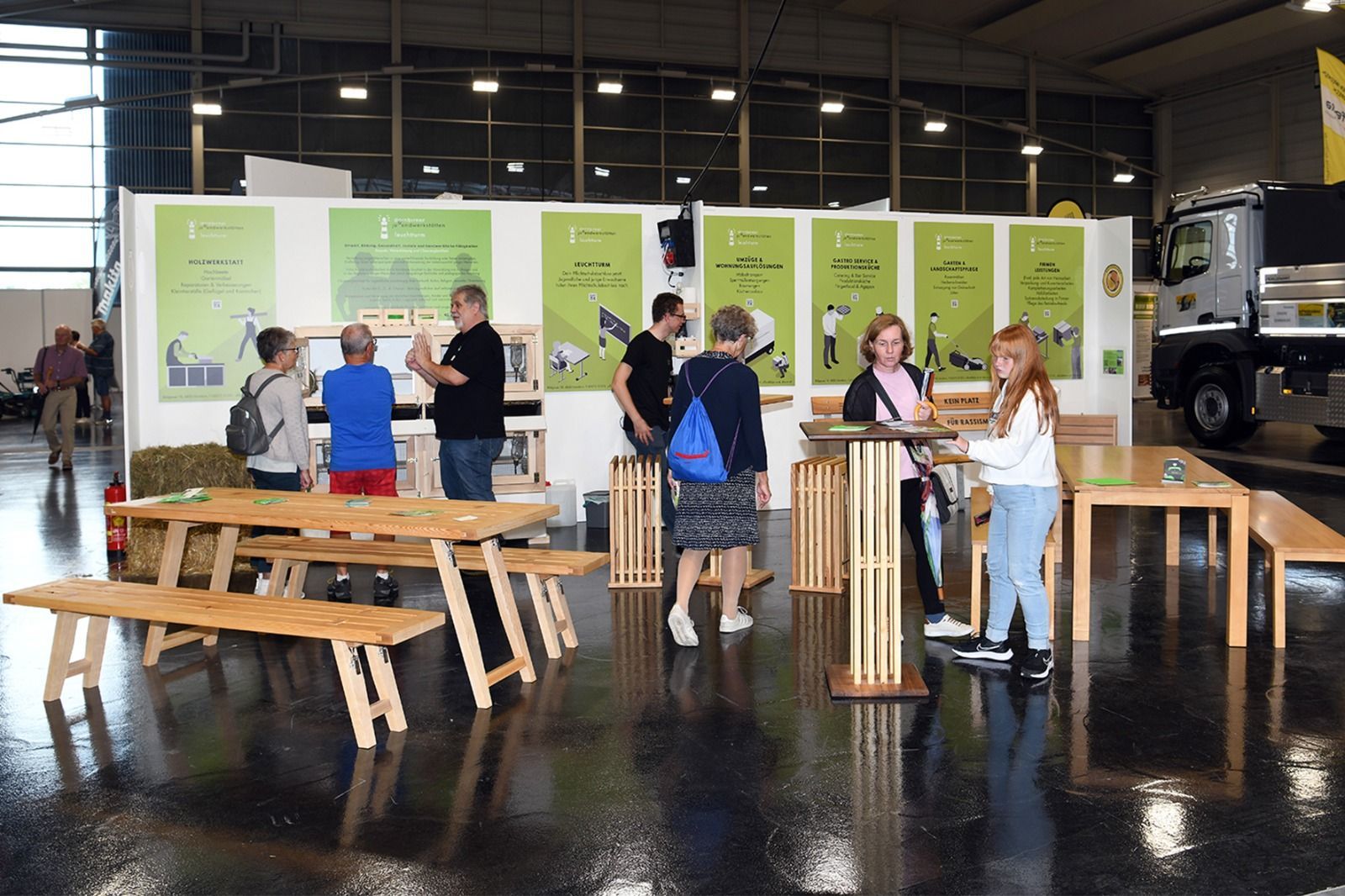 Eine Gruppe von Menschen, die in einem Raum um Tische und Bänke herumstehen