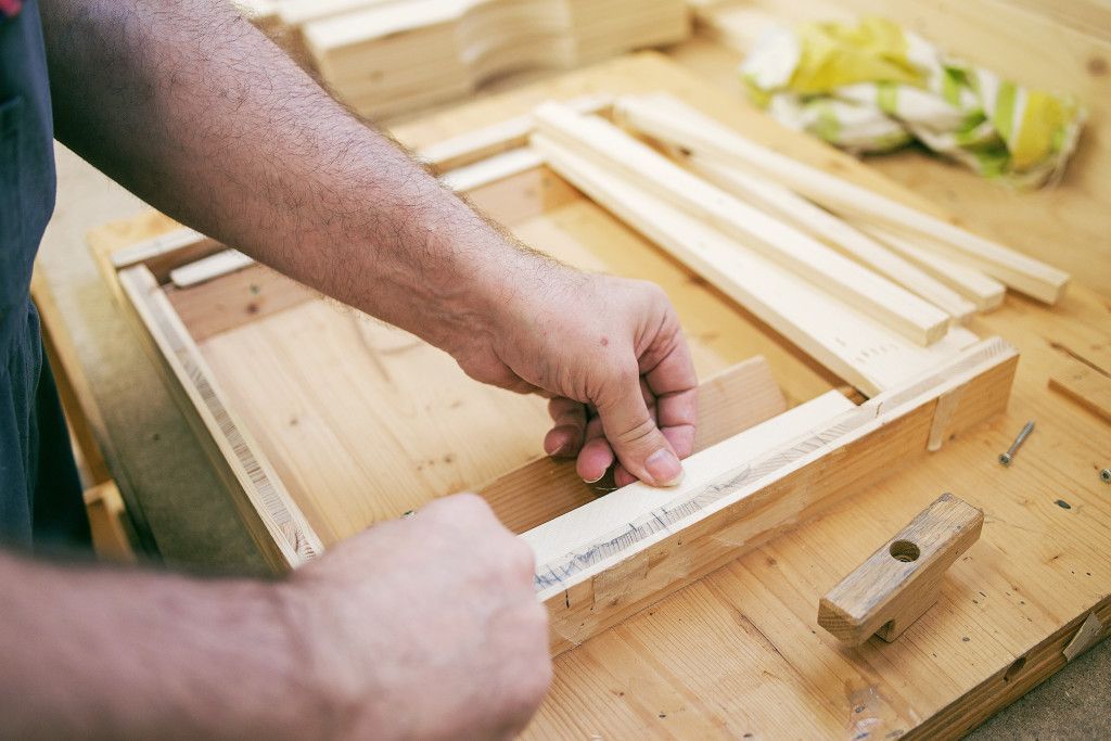 Ein Mann arbeitet an einem Holzrahmen auf einem Holztisch.
