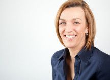 Eine Frau in einem blauen Hemd lächelt in die Kamera.