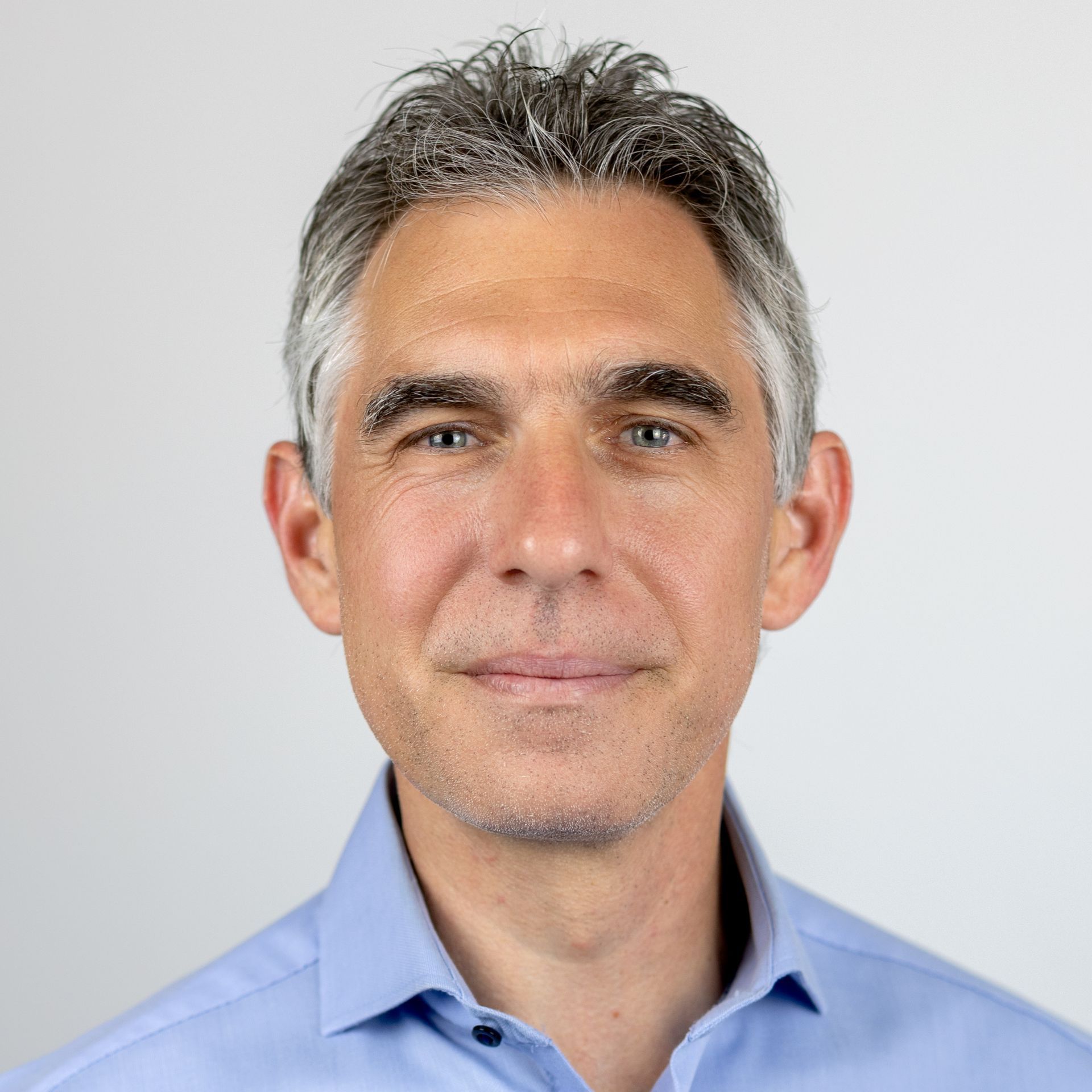 Ein Mann mit grauem Haar und blauem Hemd lächelt in die Kamera.