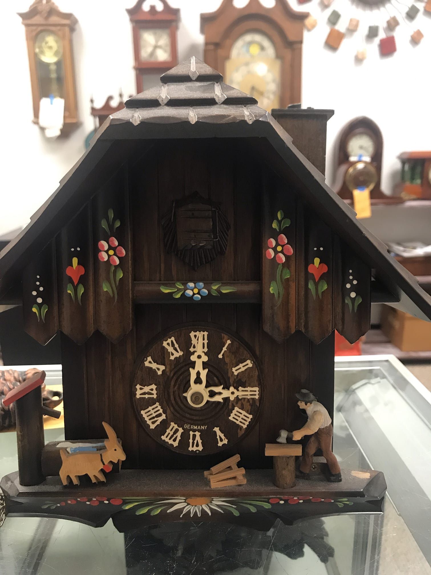 A cuckoo clock with roman numerals is sitting on a glass table.