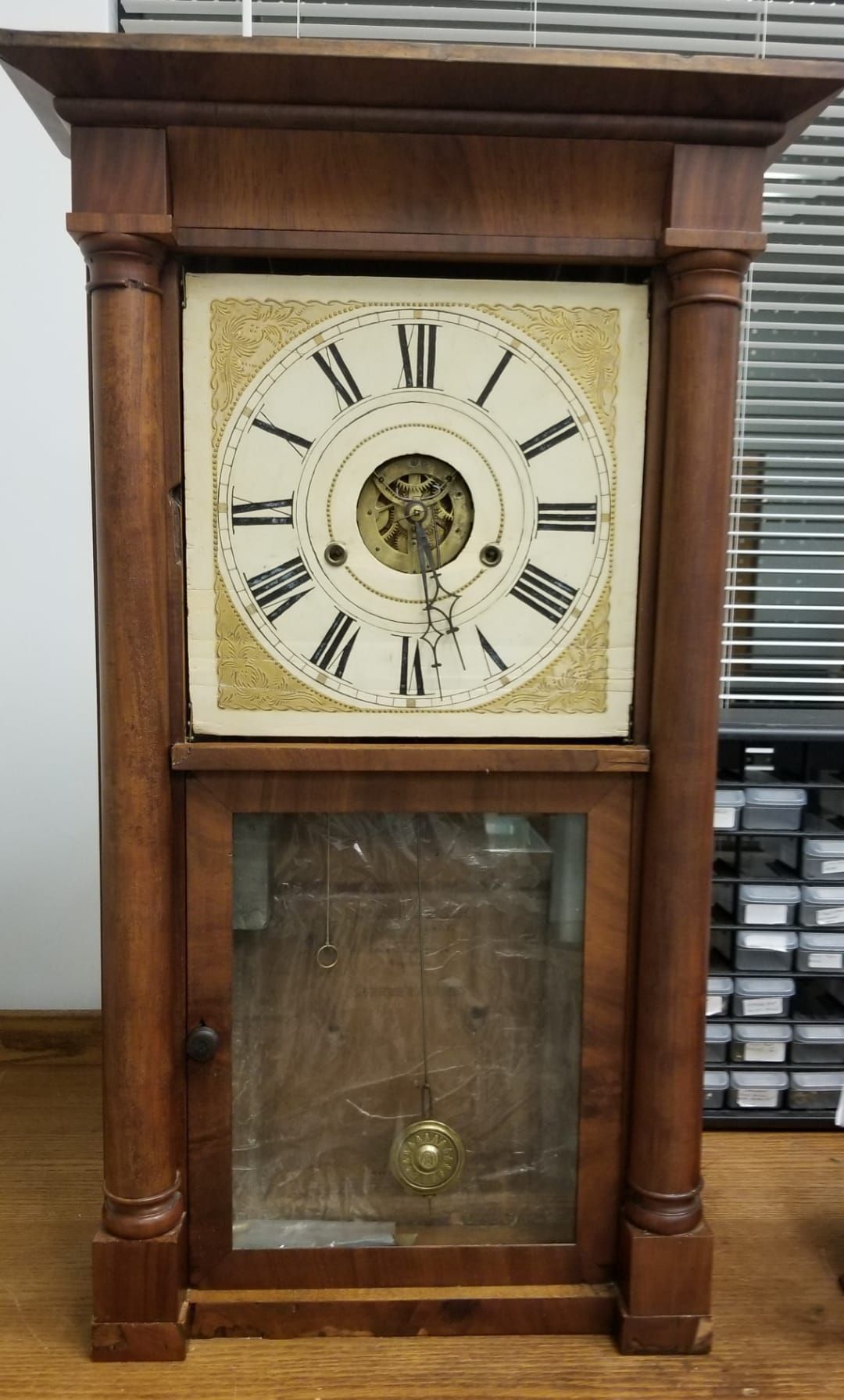 A wooden clock with roman numerals is sitting on a wooden floor.