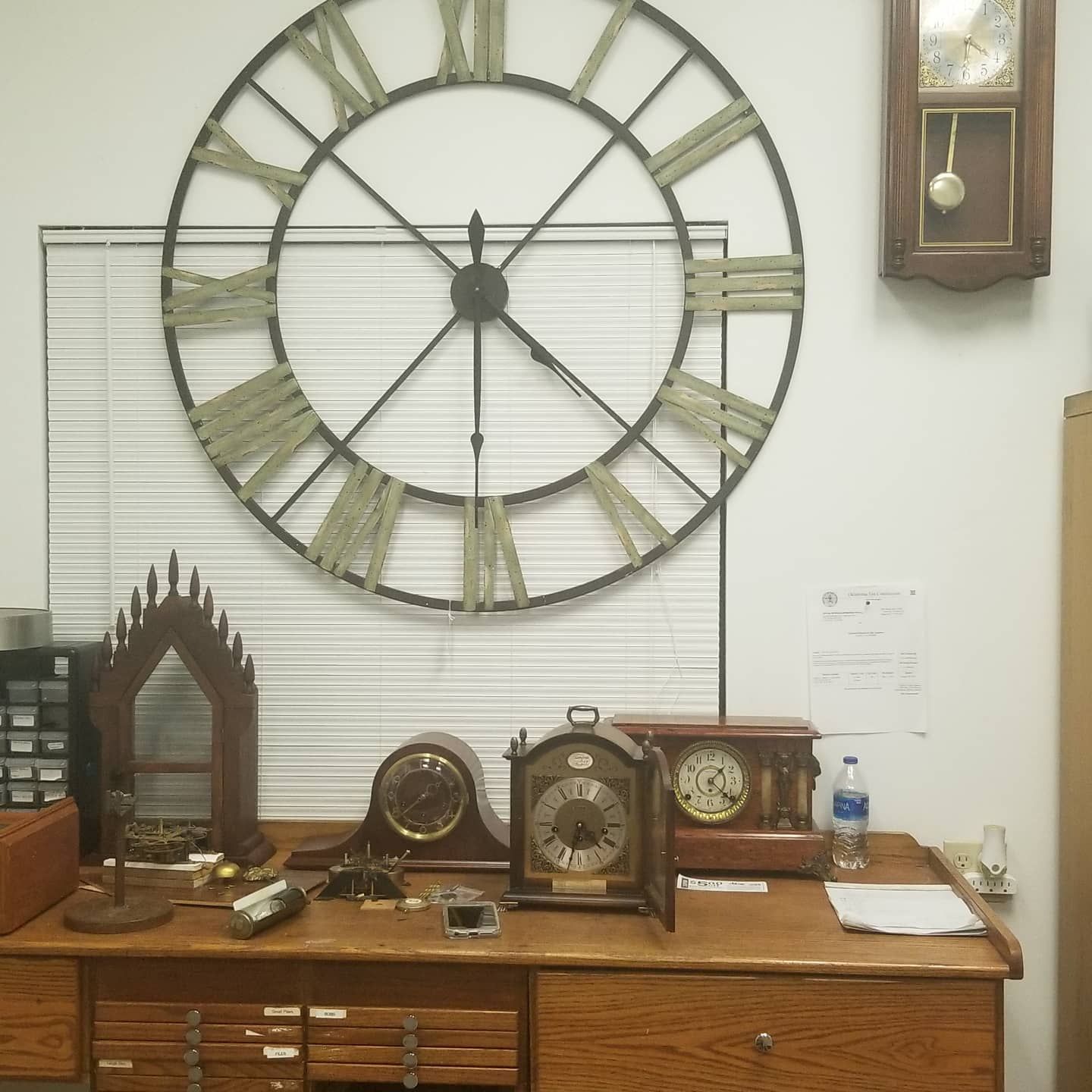 A large clock with roman numerals hangs above a desk
