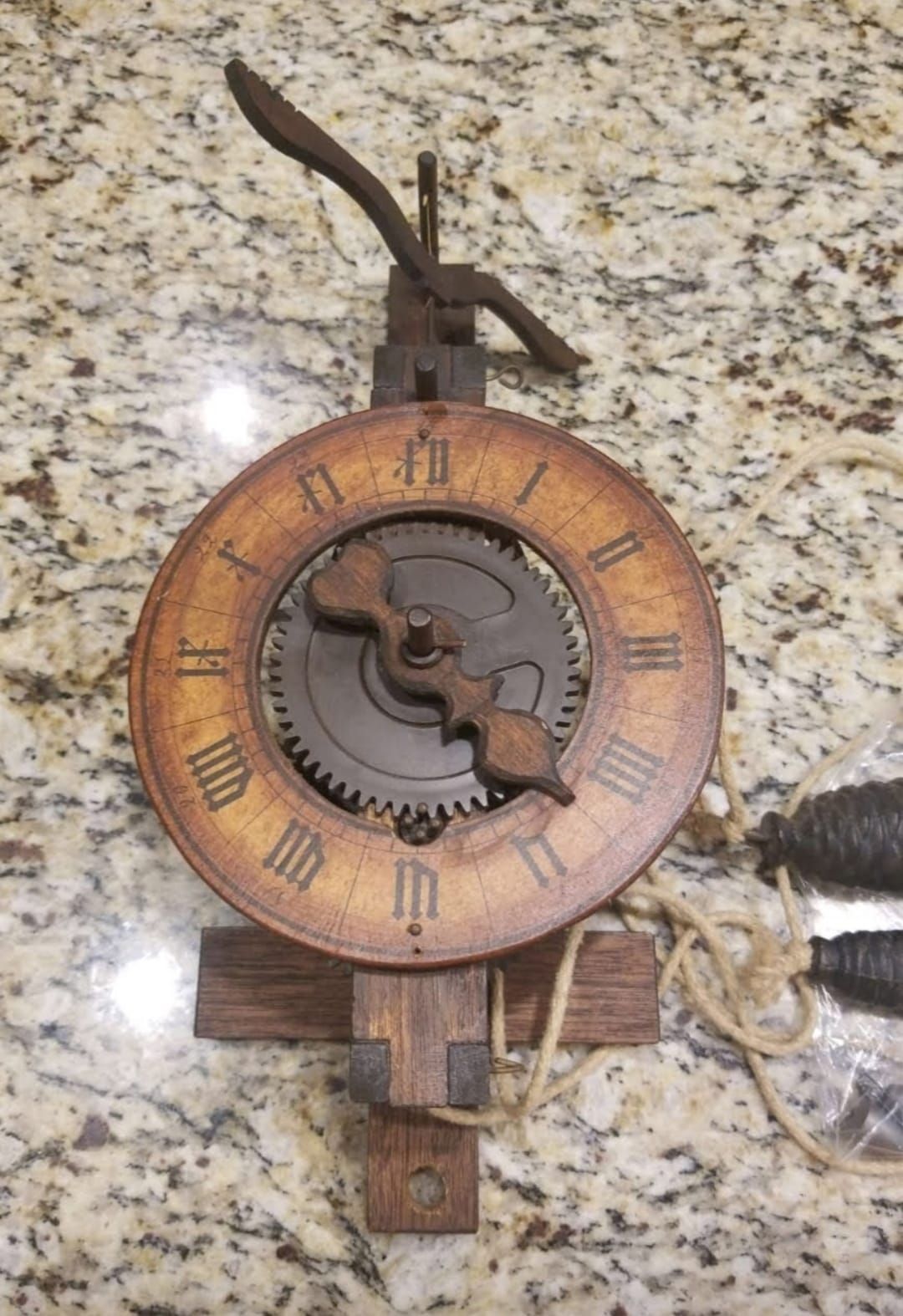 A wooden clock with roman numerals is sitting on a granite counter.