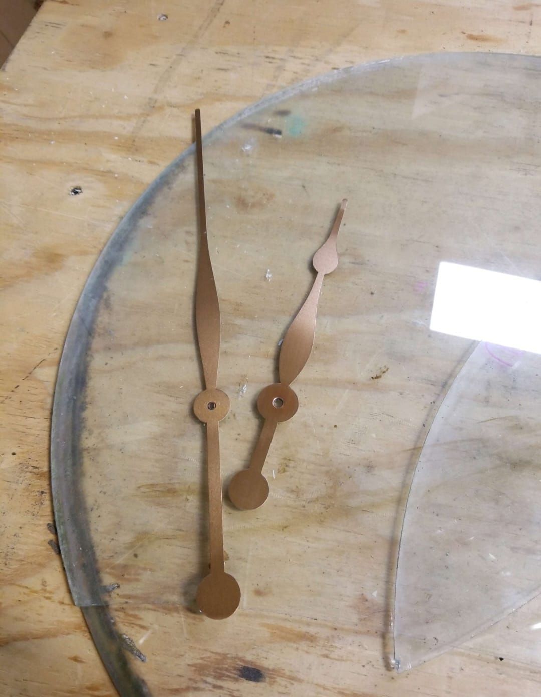 A pair of clock hands are sitting on top of a wooden table.