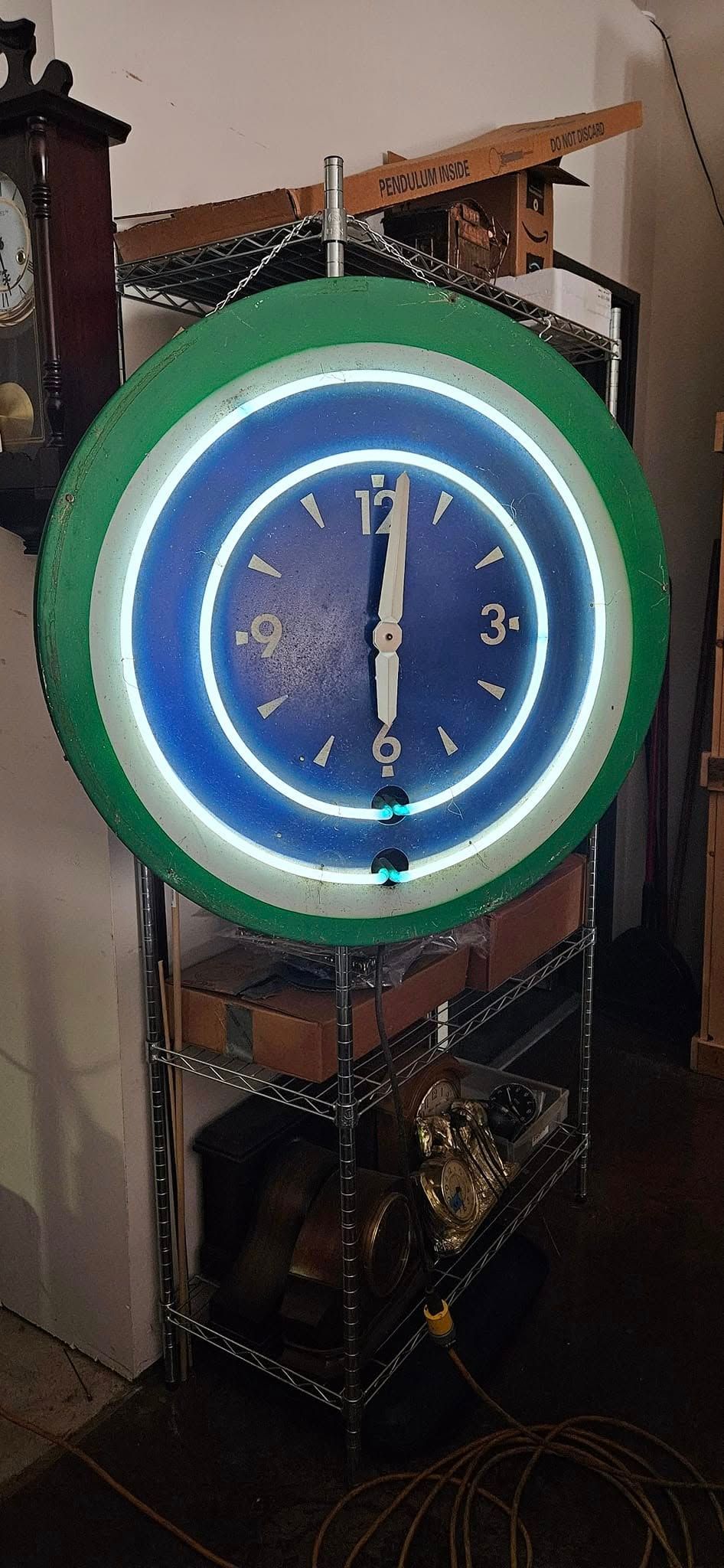 A neon clock is hanging on a metal rack in a room.