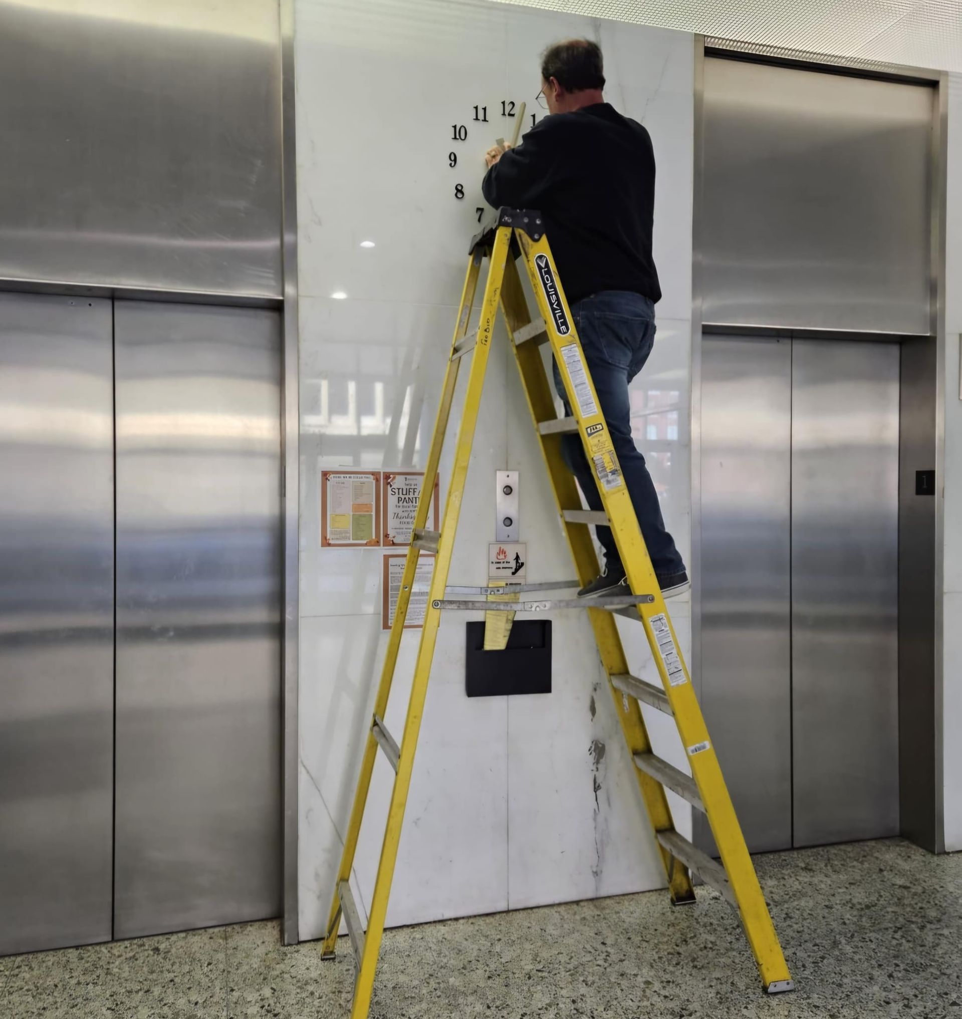 A man standing on a ladder fixing a clock