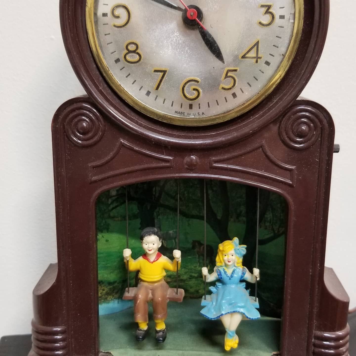 A clock with a boy and a girl sitting on swings