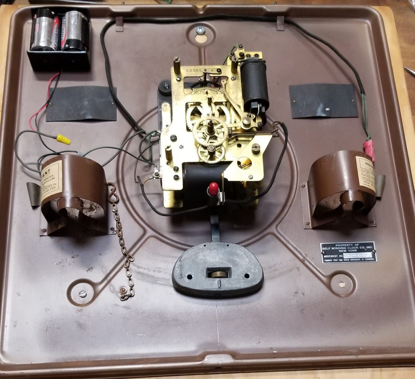 A clock is sitting on a brown tray with a battery in it